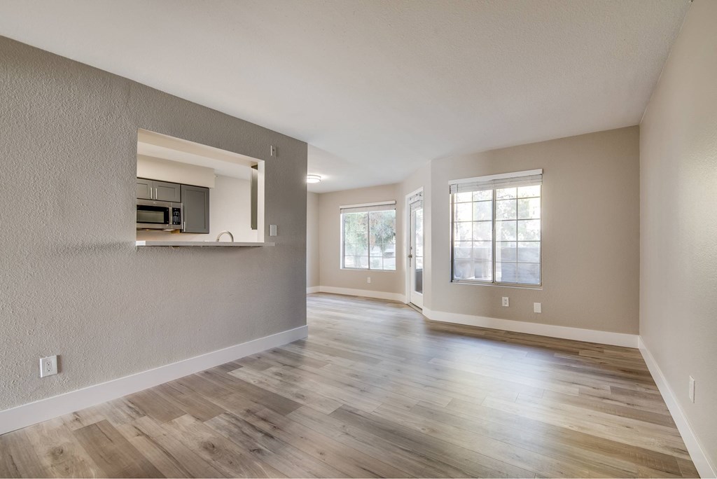 A spacious room with wooden flooring and a kitchen area in the background.