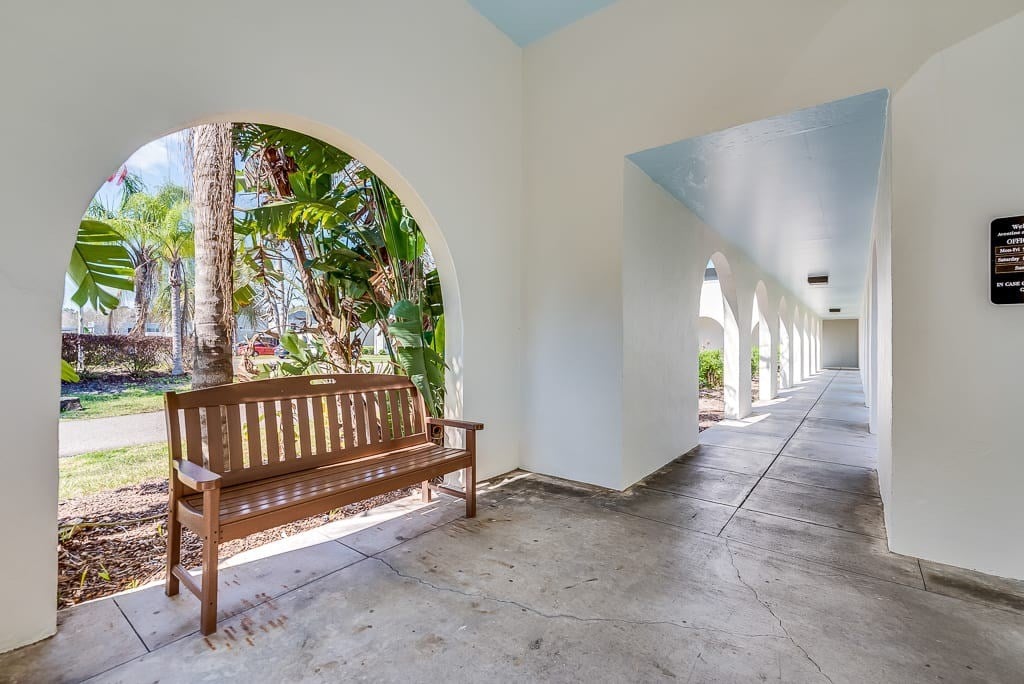 A wooden bench sits in a white hallway with a view of trees through an arched window.