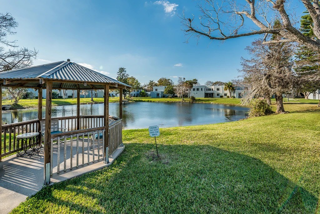 A gazebo sits in a grassy area next to a lake.