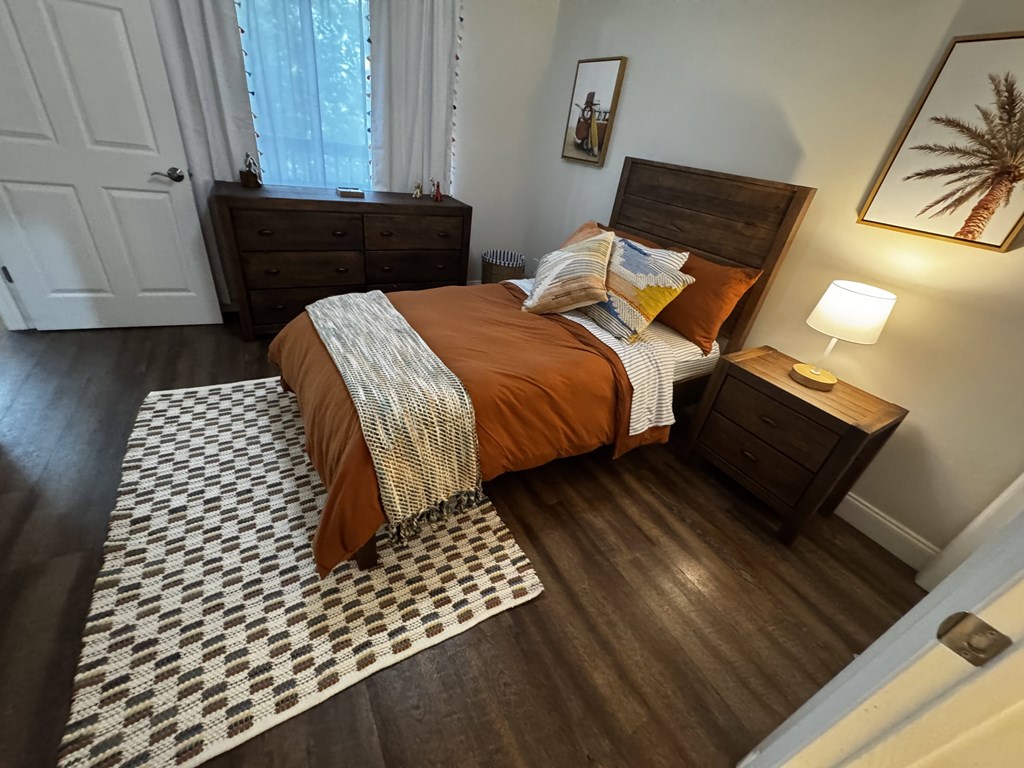 A bedroom with a bed, nightstand, and a painting of a palm tree on the wall.