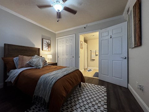 A bedroom with a bed, a ceiling fan, and a doorway leading to another room.