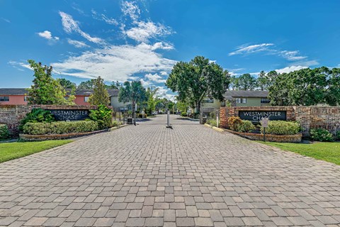 A brick pathway leads to a building with a sign at Westminster Chase Apartments, Tampa, FL, 33616