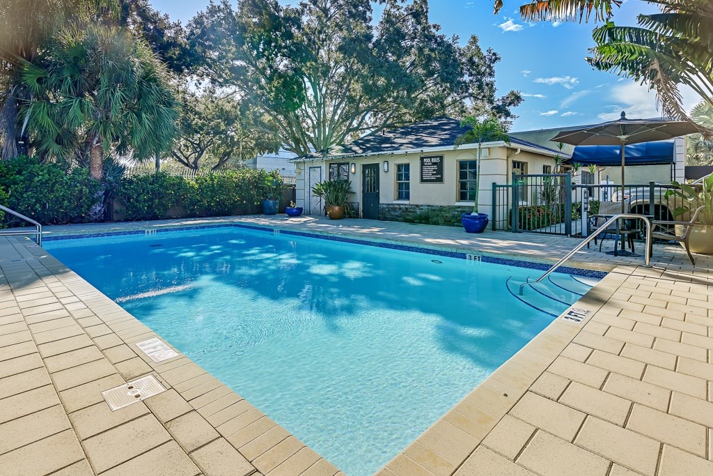 A swimming pool surrounded by a brick patio and trees.