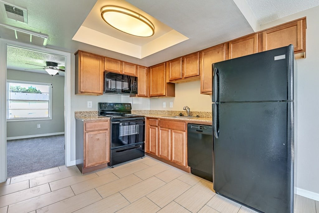 A black refrigerator is in a kitchen with wooden cabinets.