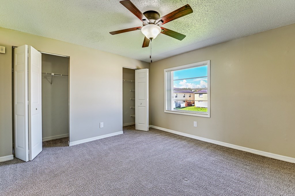 A room with a ceiling fan and a window showing a view of a house.