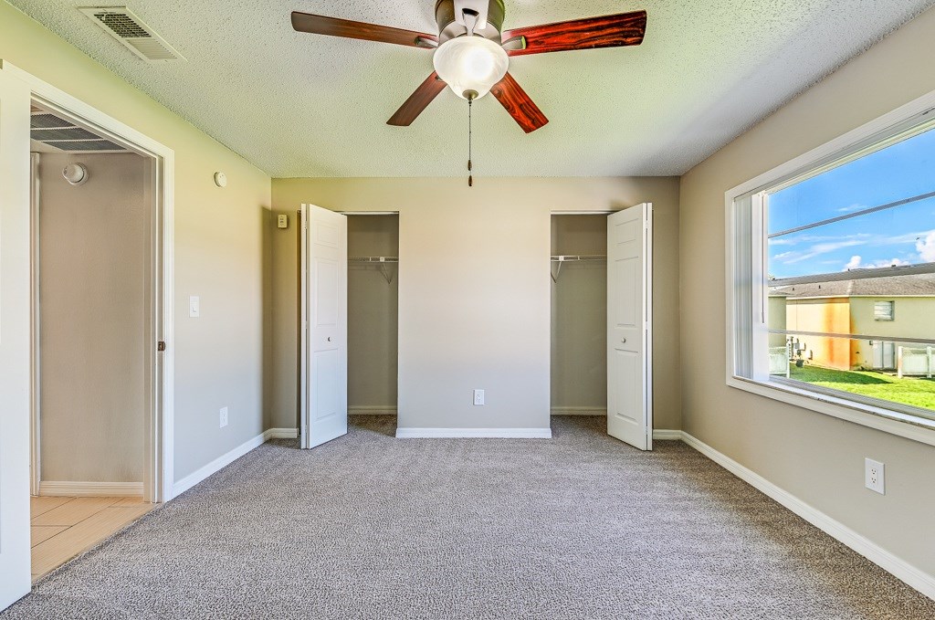 A room with a ceiling fan and a window overlooking a building.
