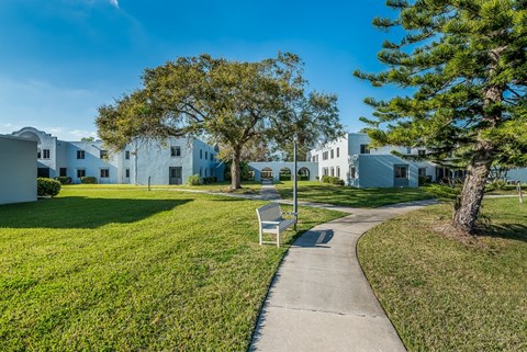 a bench sits on the grass in front of a row of white apartment buildings