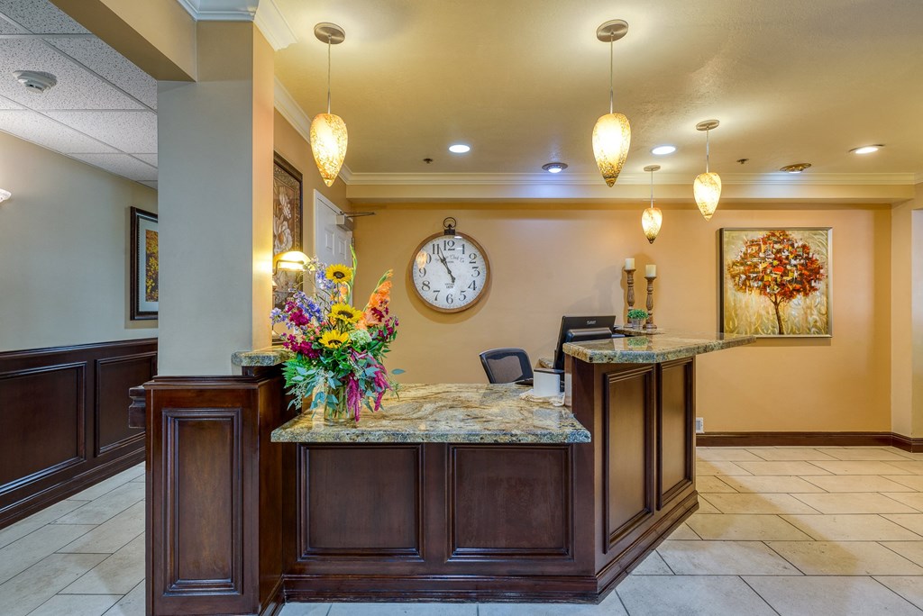 a lobby with a large clock on the wall and a reception desk with a bunch of flowers
