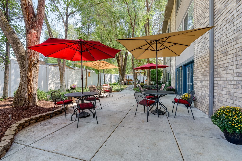 a patio with tables and umbrellas in front of a brick building