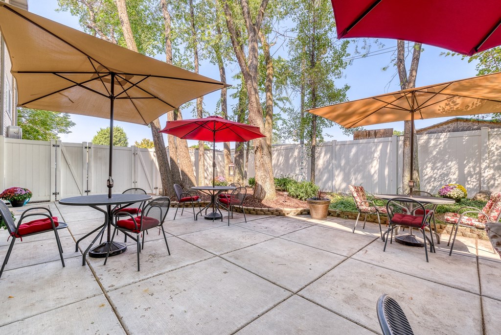 a patio with tables and umbrellas at the whispering winds apartments in pearland, tx