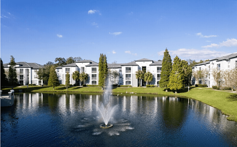 A fountain in the middle of a pond in front of a building.
