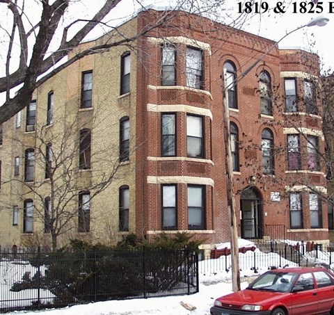 A red car is parked in front of a large brick building.