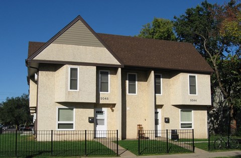 a tan brick house with a fence in front of it