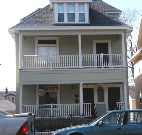 A two story house with a balcony and a car parked in front.