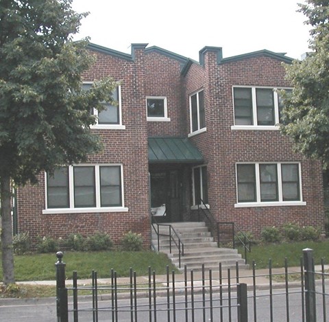 A red brick house with a green awning and a black fence in front.