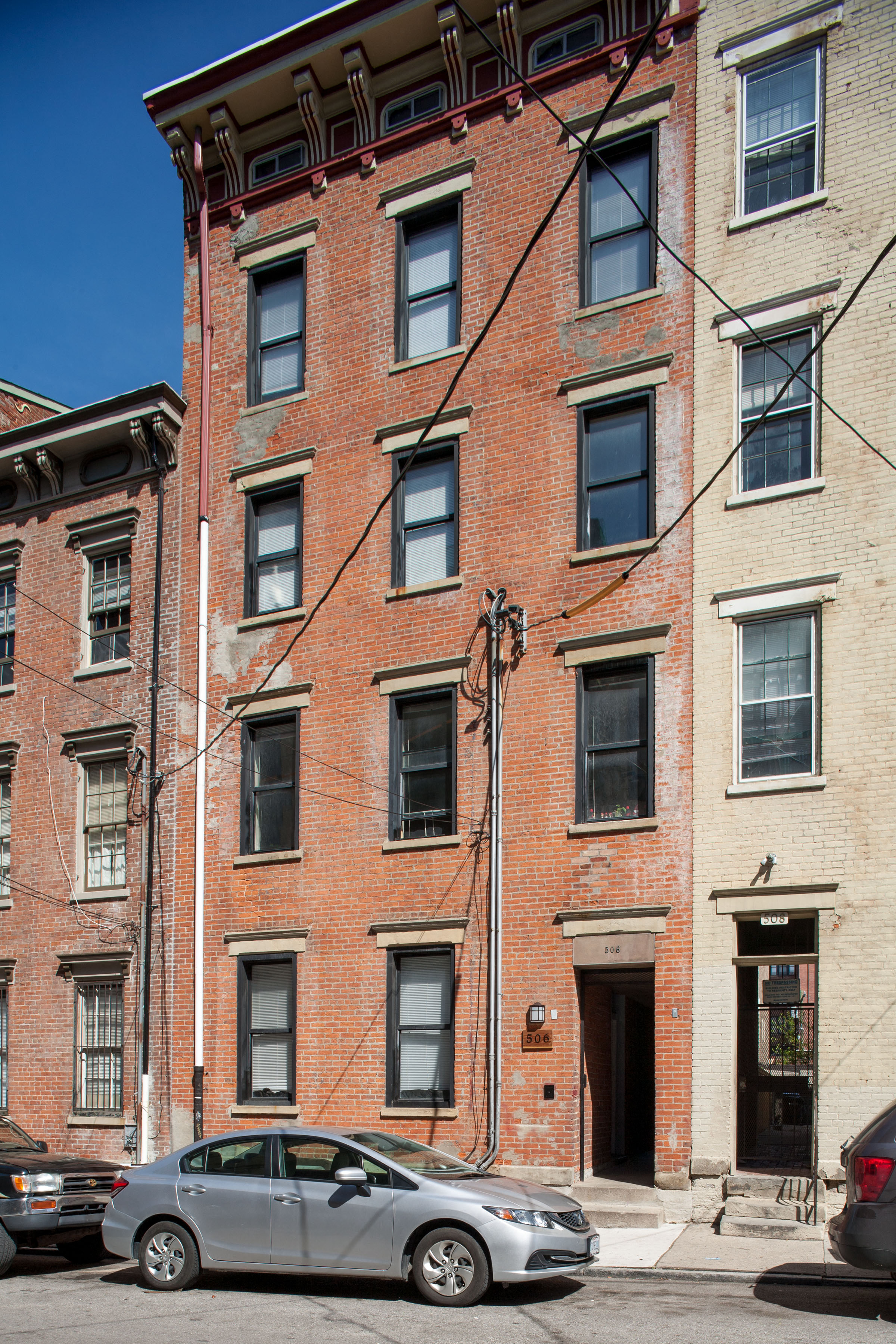 A grey car is parked in front of a red brick building.