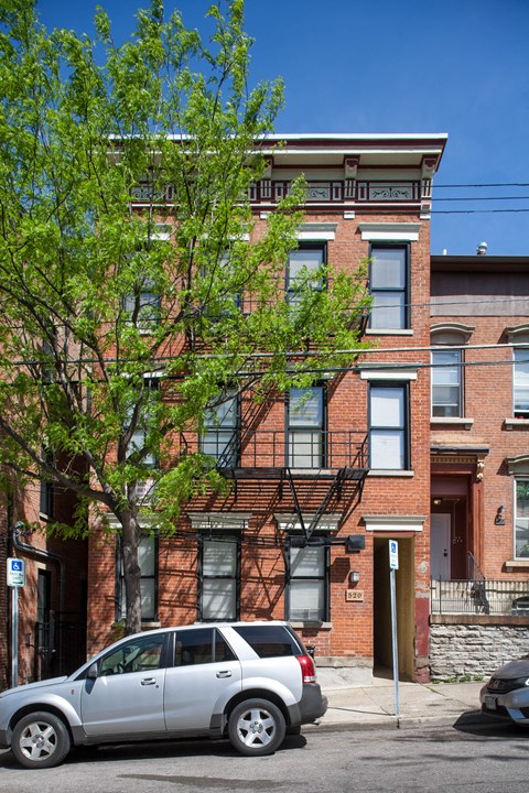 A silver car is parked on the street in front of a red brick building.