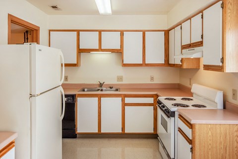 an empty kitchen with white appliances and wooden cabinets
