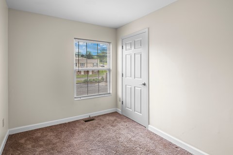 A room with a carpeted floor and a window with blinds.