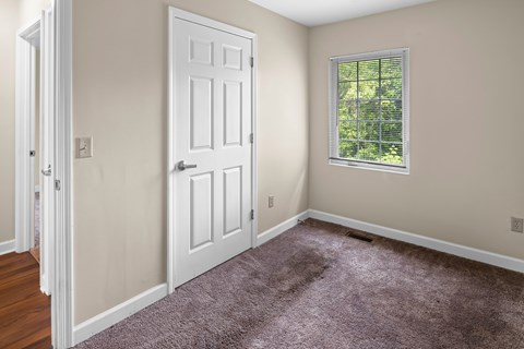 A room with a white door and a window with a view of trees.