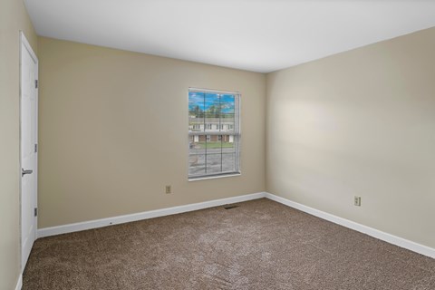 A room with a carpeted floor and a window showing a view of a building.