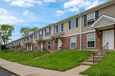A row of townhouses with green lawns and trees in the background.