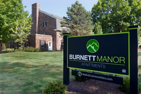 A sign for Burnett Manor Apartments stands in front of a brick building.