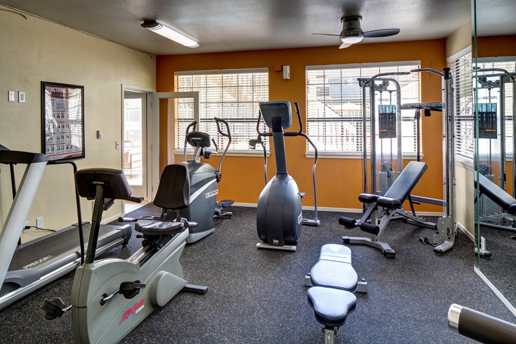 a gym with cardio equipment and weights with orange walls at 2000 Lake Washington Apartments, Washington