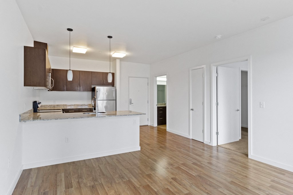 an empty living room with a kitchen and a door to a hallway at The Parker Apartments, Portland, 97209