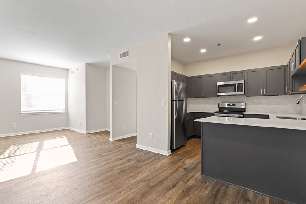 an empty living room with a kitchen with stainless steel appliances at Switchback on Platte Apartments, Littleton, CO 80120