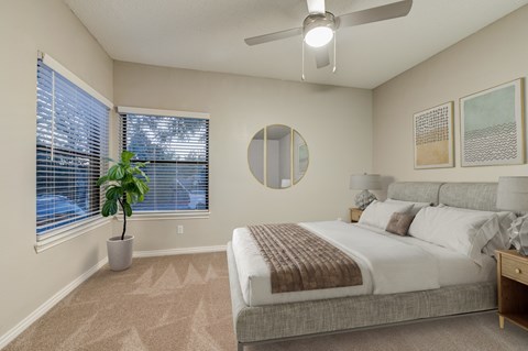 A bedroom with a large bed, a potted plant, and a ceiling fan.