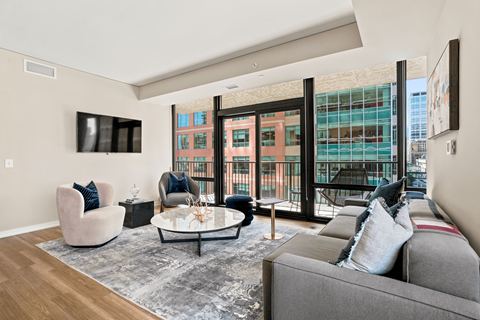 A living room with a grey couch, a white coffee table, and a large window with a view of a building.