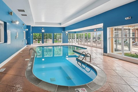 A large indoor swimming pool with a blue tiled floor and a glass wall.