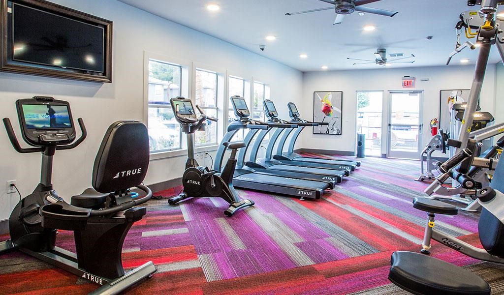 a gym with cardio equipment and a tv on the wall