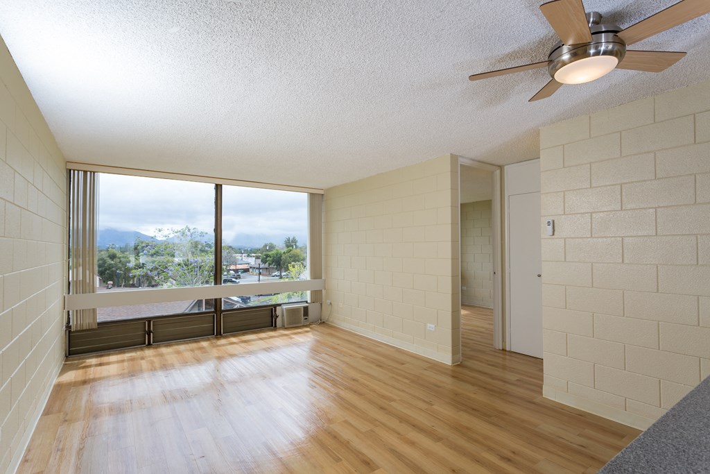 an empty living room with wood floors and a large window at Palms of Kilani Apartments, Wahiawa, HI, 96786