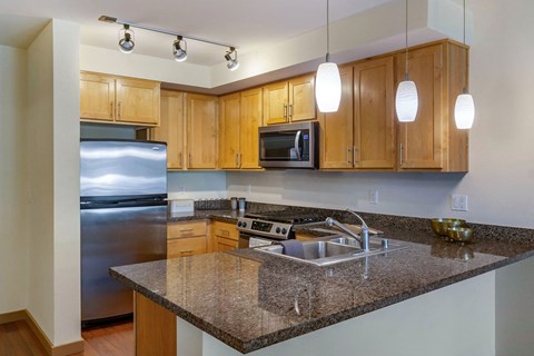a kitchen with granite countertops, pendant lighting, and wooden cabinets at 128 on State, Kirkland, 98033