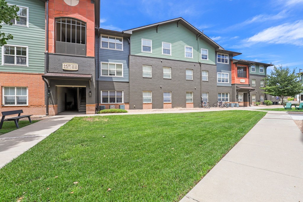 a sidewalk in front of an apartment building with a lawn at Switchback on Platte Apartments, Littleton, CO