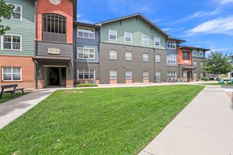 a sidewalk in front of an apartment building with a lawn at Apartments at Denver Place,Denver, CO 80202