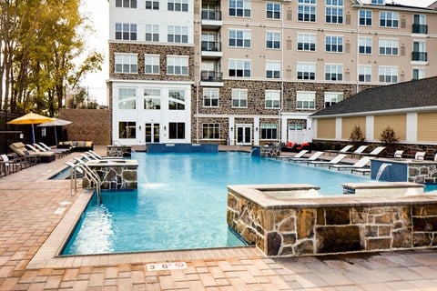 a pool with a stone wall and lounge chairs in front of a building at Heights at Glen Mills, Glen Mills