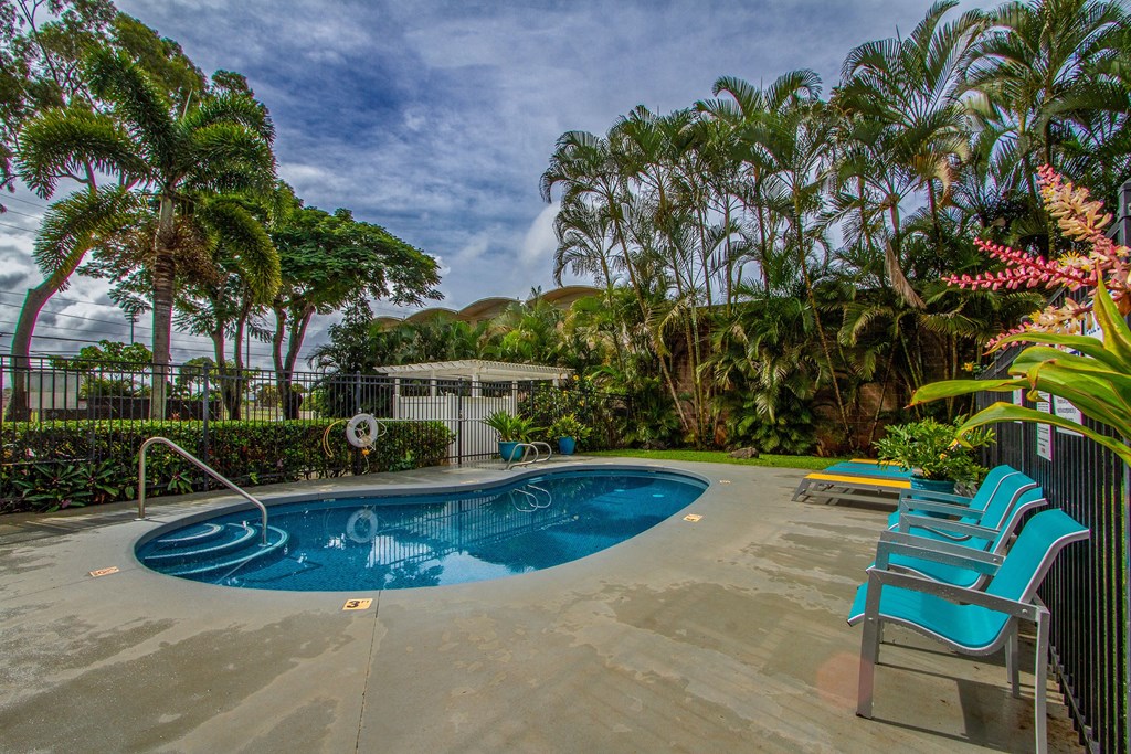a swimming pool and chairs in a backyard with palm trees at Palms of Kilani Apartments, Wahiawa, HI 96786