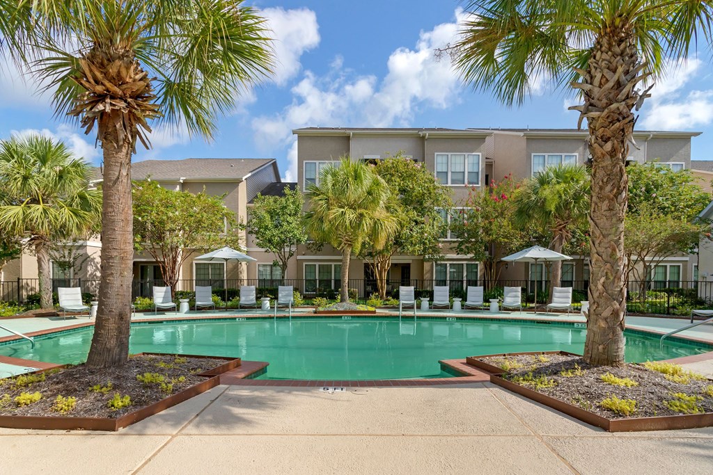 a swimming pool with palm trees and a building in the background at Summerwind, Pearland, TX 77584