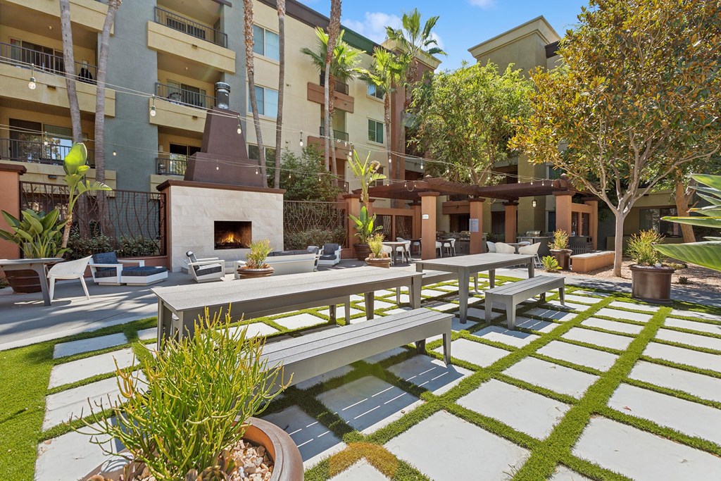A patio with a table and chairs is surrounded by a grassy area and apartment buildings at The Kitt at Warner Center Apartments, California, 91303