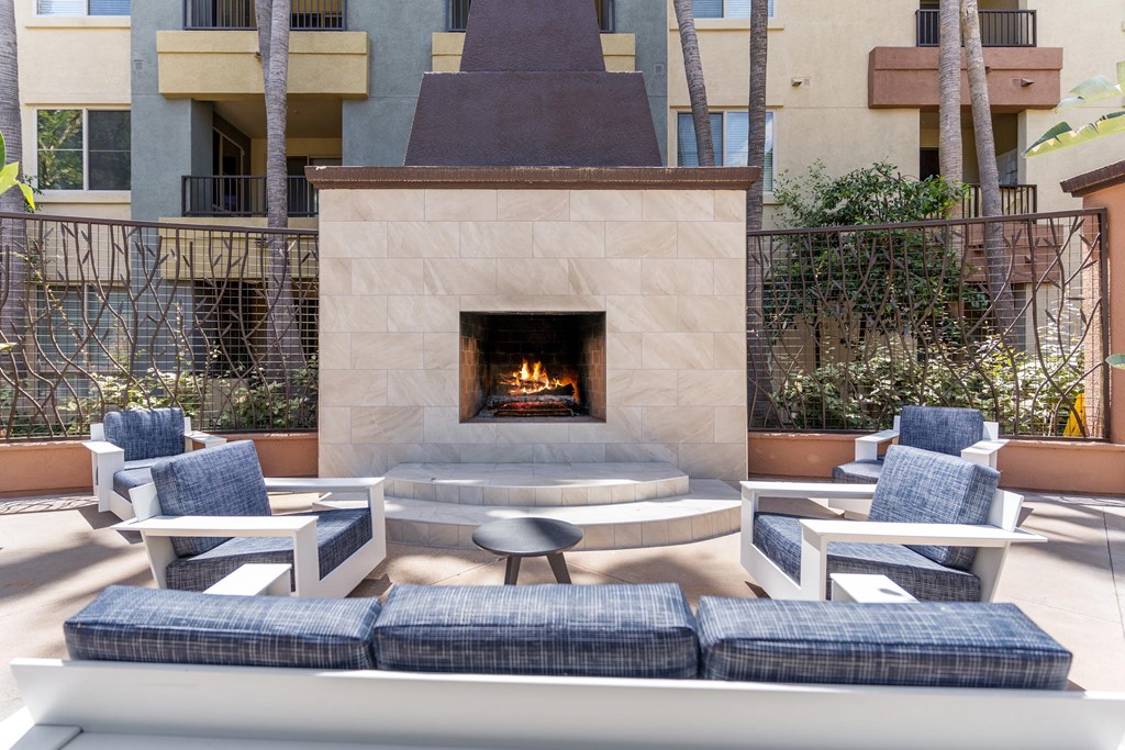 A fireplace is in the middle of a patio with blue cushioned chairs around it at The Kitt at Warner Center Apartments, California, 91303