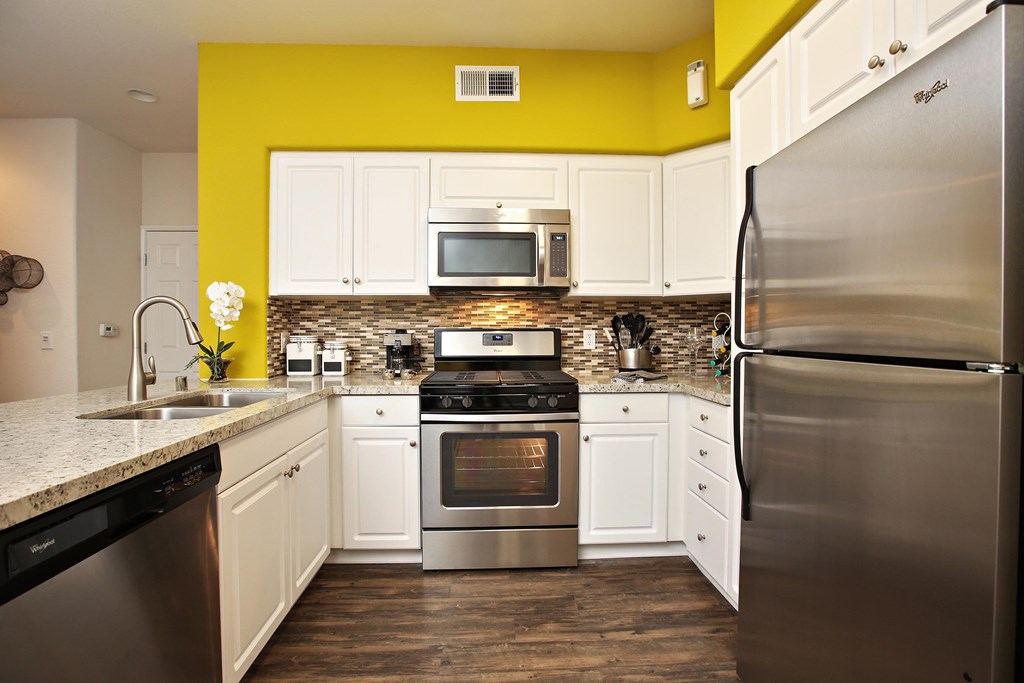 A kitchen with a yellow wall and stainless steel appliances at The Kitt at Warner Center Apartments, California, 91303