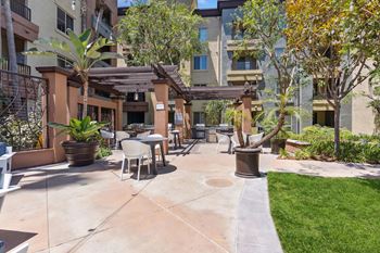 A patio area with a table and chairs surrounded by plants and trees. at The Kitt at Warner Center Apartments, Woodland Hills, CA, 91303