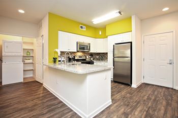 A kitchen with white appliances and a yellow accent wall. at The Kitt at Warner Center Apartments, Woodland Hills, California