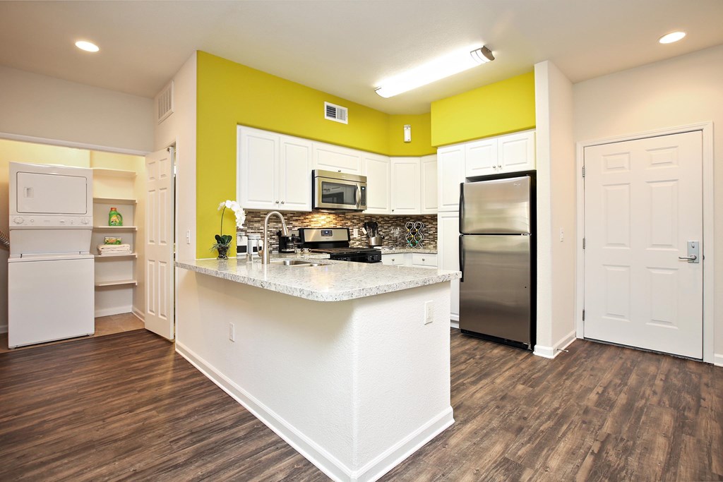 A kitchen with white appliances and a yellow accent wall at The Kitt at Warner Center Apartments, Woodland Hills 91303