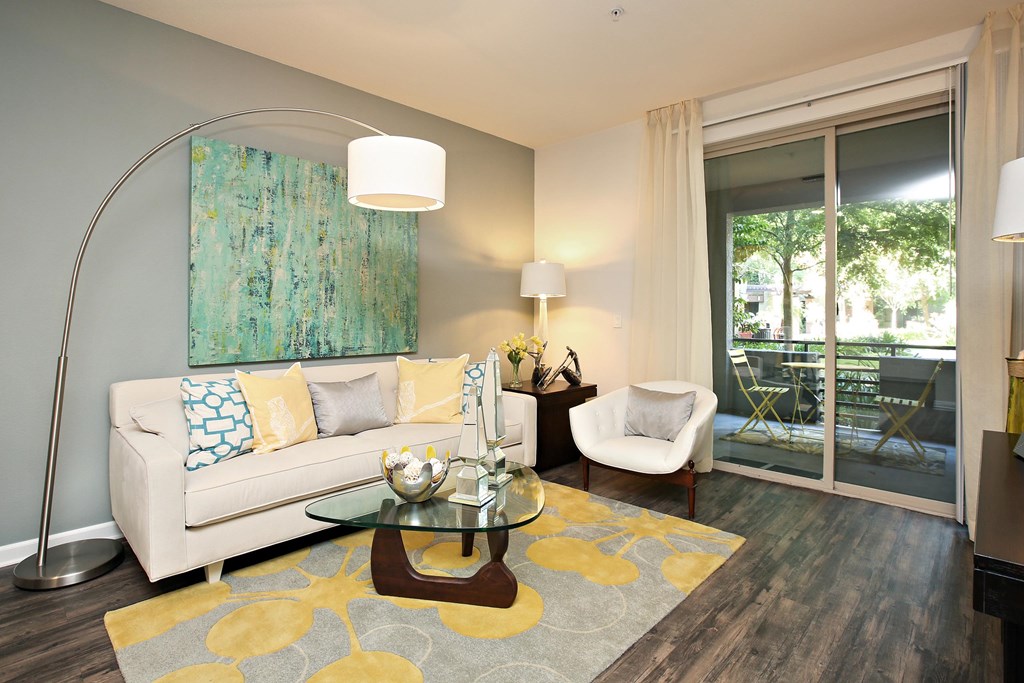 A living room with a white couch, a glass coffee table, and a painting on the wall at The Kitt at Warner Center Apartments, Woodland Hills, California