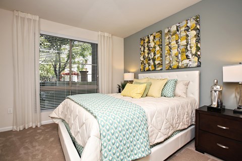 A bedroom with a large bed and a window with blinds. at The Kitt at Warner Center Apartments, Woodland Hills, California