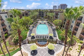 A pool surrounded by palm trees and umbrellas at The Kitt at Warner Center Apartments, California